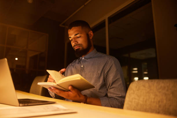 istock Young businessman working overtime at a desk in a dark office 1454198541