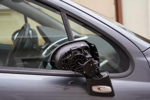 Close up view on broken adjustable door back mirror or wing mirror made from black plastic. From the removed cover sticking out electrical red and blue cables. Partly is visible defocused interior.