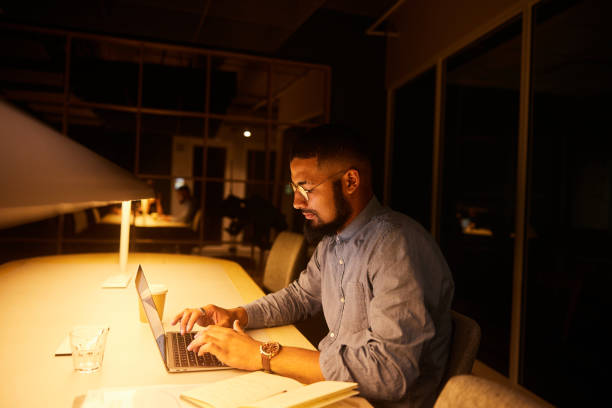 istock Young businessman working on a laptop in a dark office 1454198792