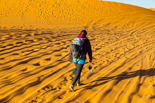 Woman tourist walking along sand dunes in the desert, Merzouga, Erg Chebbi sand dunes region, Sahara, Morocco. Model released.