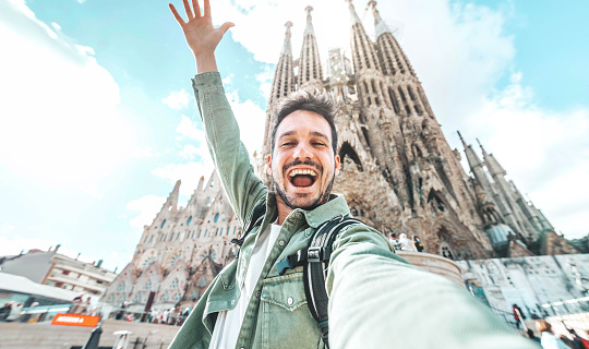 Happy tourist visiting La Sagrada Familia, Barcelona Spain - Smiling man taking a selfie outside on city street - Tourism and vacations concept