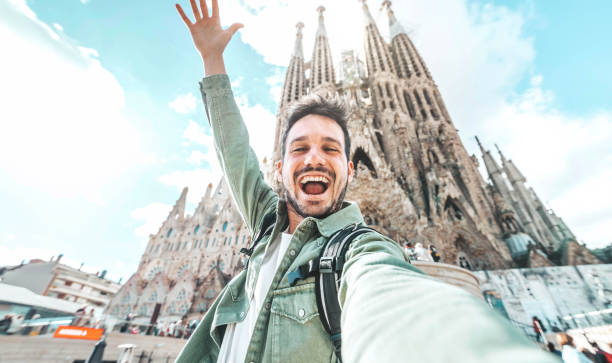 Happy tourist visiting La Sagrada Familia, Barcelona Spain - Smiling man taking a selfie outside on city street - Tourism and vacations concept stock photo