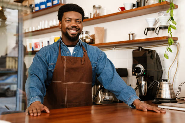 istock Black bearded man wearing apron smiling while working in cafe 1454203797