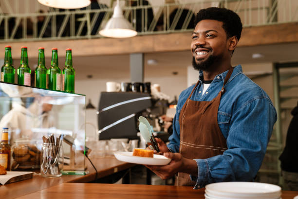 istock Black bearded man wearing apron laughing while working in cafe 1454203942