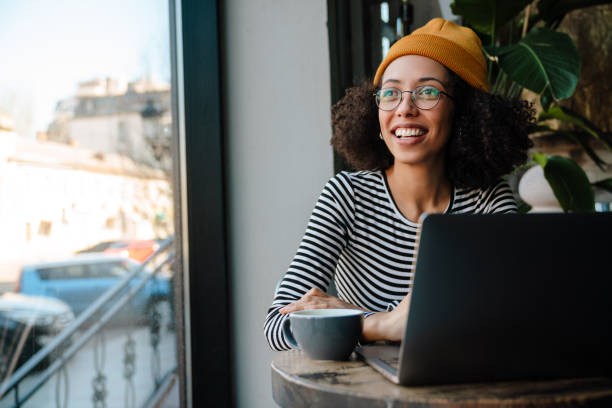 istock Young african american woman smiling and using laptop computer in cafe 1454204101
