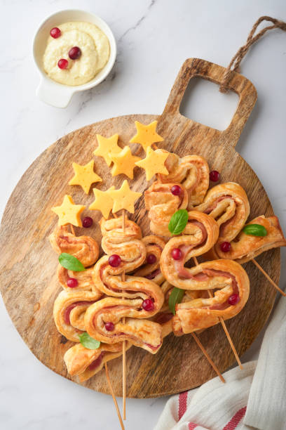 istock Christmas or New Year appetizer. Christmas tree shape puff pastry buns with cheese and ham. Group of Christmas tree shapes on wooden board. Festive idea for Christmas or New Year dinner. Top view. 1454204632