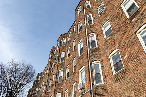 Brick face with rows of windows in multi story brick apartment building, urban cityscape, horizontal aspect