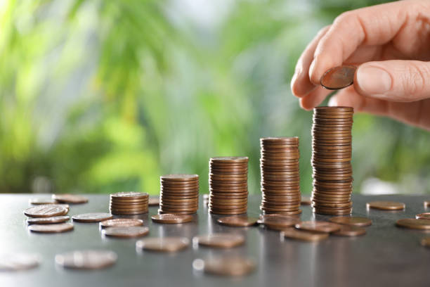 istock Woman stacking coins at grey table against blurred green background, closeup. Space for text 1454205485