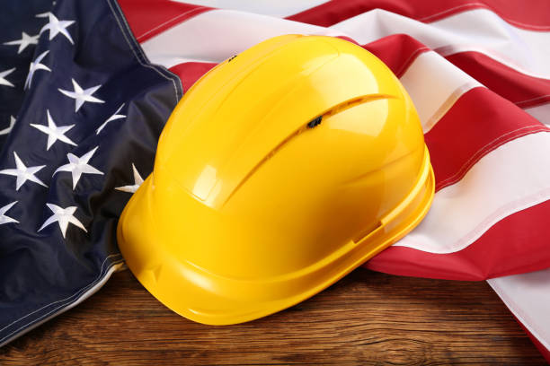 istock Yellow protective hard hat and American flag on wooden table 1454205575