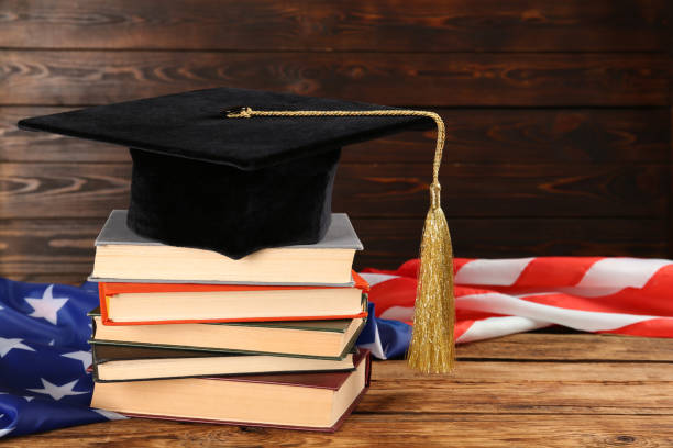 istock Graduation hat, books and American flag on wooden table. Space for text 1454206500