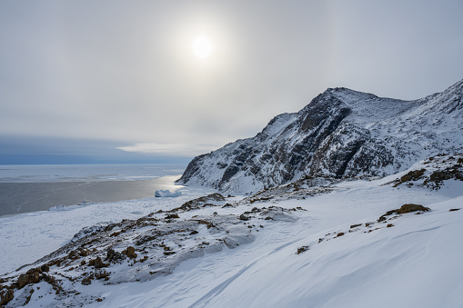 View over the pack ice on the north atlantic ocean near Tasiilaq, located in East Greenland. Around the sun is a halo visible.