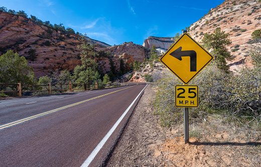 Aerial view overlooking a straight road and epic mountains in the Zion National Park, Utah, USA. Warning sign warning for a steep turn to the left.