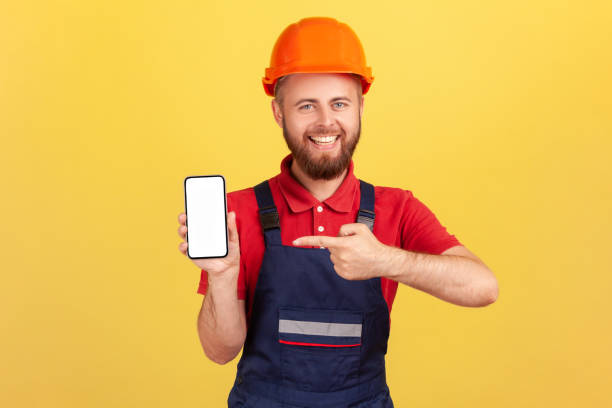 istock Builder man or repairman in uniform and protective helmet showing cell phone with blank empty screen 1454209148