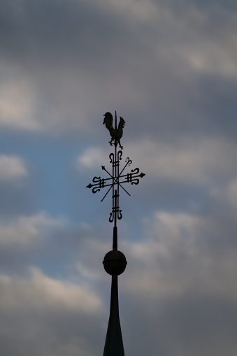A vertical shot of a cross and a weather vane on a church roof