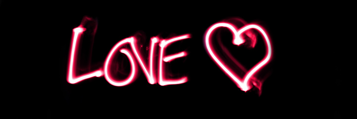 Word love white a heart in pink on panoramic black background.Valentines day, love light painting.