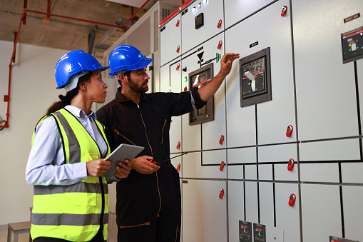 Male and Female colleague electrical engineer work checking at Electrical Distribution Control Room