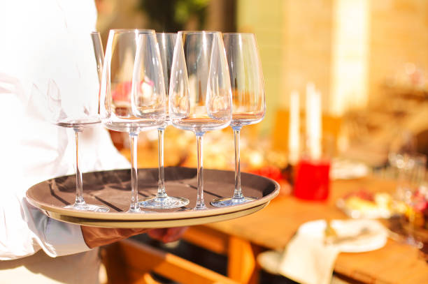 istock Waiter carrying tray with empty wine glasses while working in outdoor restaurant 1454212372