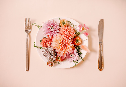 Top view of fork and knife cutting and plate with natural flowers on plate against peach background