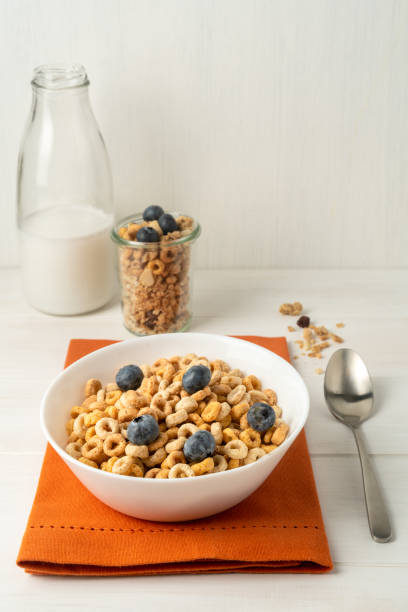 istock Cereal bowl, milk bottle and spoon on an orange napkin on a white table, front view 1454221577