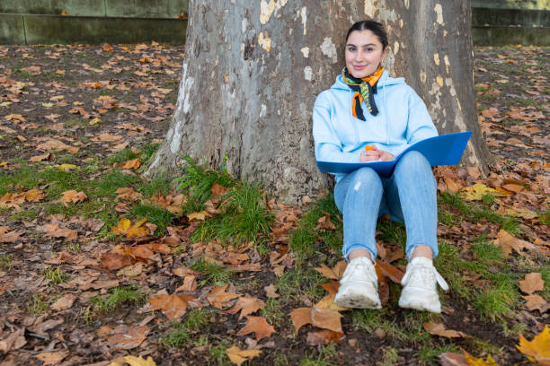fille orientale assise sous un arbre avec un dossier bleu dans ses mains, autriche - fall semester photos et images de collection