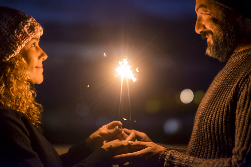 Happy couple celebrate together with love and romance in the new year eve night firing sparklers. Man and woman enjoy magic moment relationship. Mature people aging forever married concept lifestyle