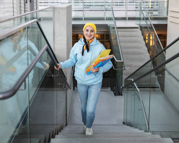 eine studentin mit hellen ordnern in den händen steigt die treppe hinauf und lächelt in die kamera, foto aus dem oberen winkel. - fall semester stock-fotos und bilder