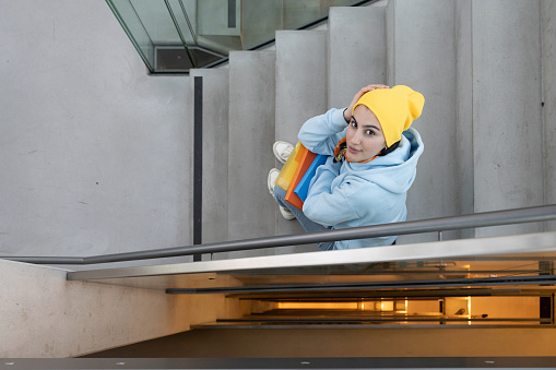 A girl with colored folders in her hands sits on a stone staircase between floors and looks up. High quality photo