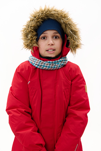 Vertical studio shot of a handsome Middle-Eastern teenage boy, wearing red down parka with fur hood and blue scarf, smiling looking at camera, over white background. Cool weather. Winter concept