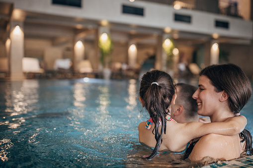 Group of people, husband and wife together in hotel swimming pool with their little daughter.