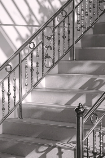 Light and shadow on surface of vintage stainless steel handrail with tile staircase outside of home in monochrome style and vertical frame