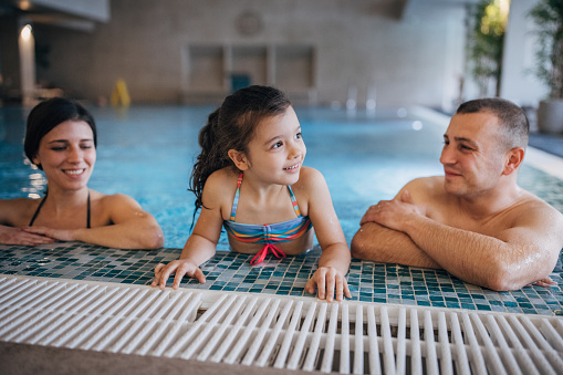 Group of people, husband and wife together in hotel swimming pool with their little daughter.