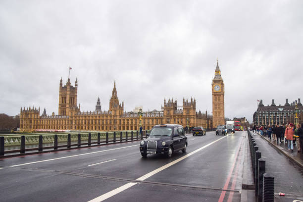 ein schwarzes taxi fährt an den houses of parliament und big ben auf der westminster bridge vorbei, london, uk - black cab stock-fotos und bilder