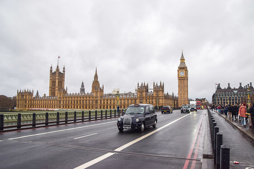 London, UK -  January 3 2023: A  black cab passes by the Houses of Parliament and Big Ben on Westminster Bridge