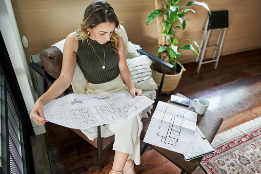 High angle view of young woman architect studying building plan drawings sitting in office