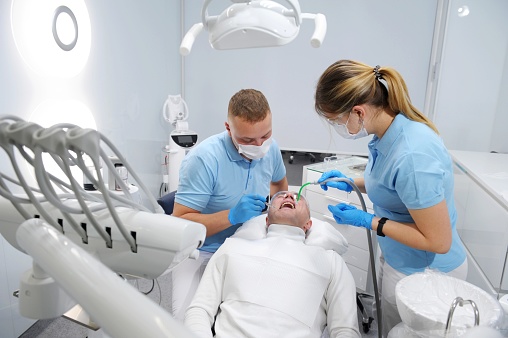 Medical treatment at the dentist office Side view of dentist talking with her patient and preparing him for the treatment. Serious man in dentist chair looking at the doctor and asking for something