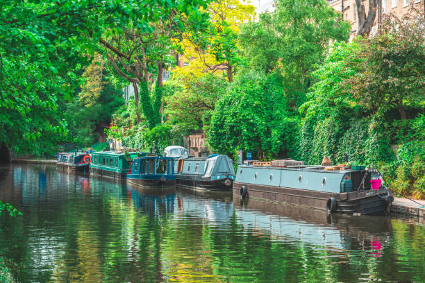 Sailing the Thames in Little Venice, London, with colorful barges under the trees on the sides Sailing the Thames in Little Venice, London, with colorful barges under the trees on the sides little venice london stock pictures, royalty-free photos & images