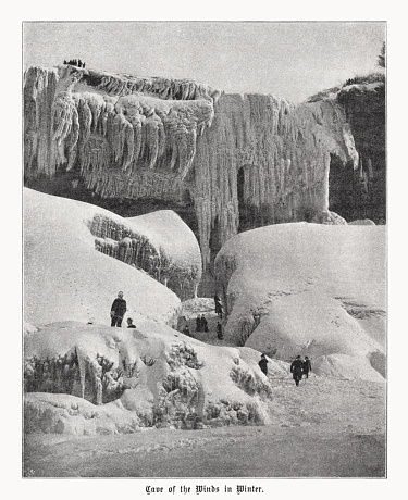 Historical view of the Cave of the Winds in winter - a natural cave behind Bridal Veil Falls at the Niagara Falls, USA. The cave was some 130 feet (40 m) high, 100 feet (30 m) wide and 30 feet (9 m) in depth. It was discovered in 1834, and originally dubbed Aeolus's Cave, after the Greek god of winds. Guided tours began officially in 1841, through Goat Island and descending down a staircase closer to the falls, into the cave. A rock fall closed the tour in 1920. It officially reopened in 1924, bringing visitors to the front of the Bridal Veil instead of behind it, on a series of decks and walkways. Tropical storm-like conditions can be experienced, as winds can reach up to 68 mph (109 km/h) underneath the falls. The cave was obliterated in a massive 1954 rockfall and subsequent dynamiting of a dangerous overhang. Halftone print after a photograph, published in 1899.