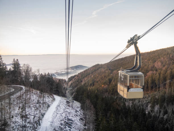Going down a cable car with panoramic winter scene landscape above the clouds. Schauinsland bahn cabins in Freiburg, Germany. Ropeway panorama descent with snow mountain peaks and valley.