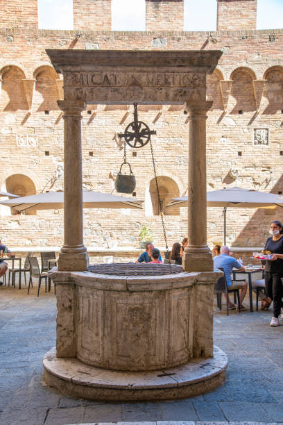 Historical fountain with chain Siena, Italy – August 24, 2020: A historical fountain with a chain and a bucket made of stone in the middle of a courtyard that is also used as an outdoor area of a restaurant. old fashioned well hand pump stock pictures, royalty-free photos & images