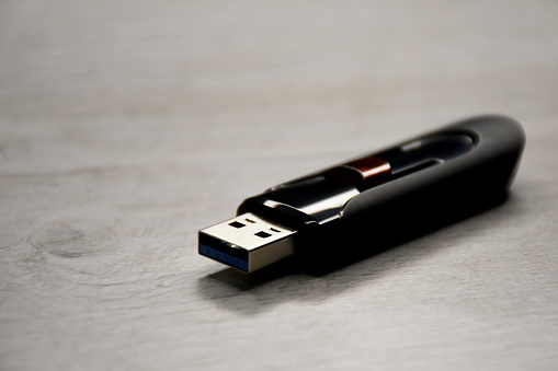 A Macro Of A Black USB Memory Stick Plugged Into The USB Port Of A Black Laptop, Side View