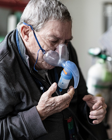 Suffering from COPD a senior man is using a nebulizer pushing liquid medication in his lungs, which will turn into a mist to help him breathe better.