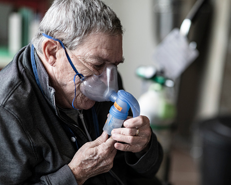 Suffering from COPD a senior man is using a nebulizer pushing liquid medication in his lungs, which will turn into a mist to help him breathe better.