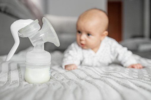 Child care concept. Breast pump with milk on background of small cute baby. Selective focus, copy space.