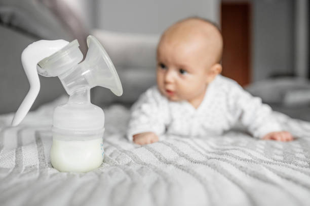 Child care concept. Breast pump with milk on background of small cute baby. Selective focus Child care concept. Breast pump with milk on background of small cute baby. Selective focus, copy space. breast milk stock pictures, royalty-free photos & images