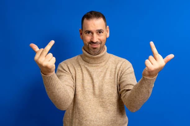 青の背景に立っているヒスパニック系の男性は、中指があなたに悪い表情、挑発、失礼な態度を犯していることを示しています。 - fuck you ストックフォトと画像