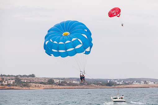 Ayia Napa, Cyprus - June 16, 2018: Parasailing in Agia Napa resort town, motor boat and blue parachute with tourists
