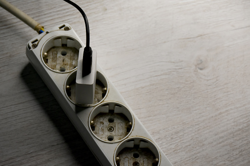 High angle view charging cable in the electrical outlet socket on the wood floor, electrical equipment