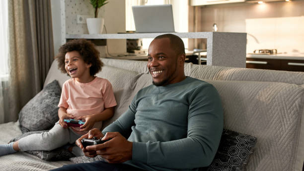 istock Little boy and father playing video game on sofa 1454249010