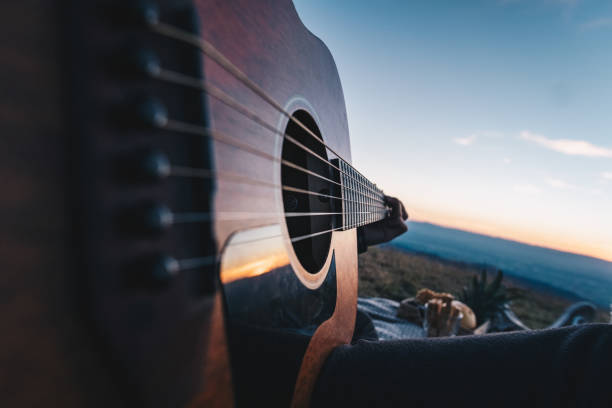 istock Young man plays guitar outdoors at twilight 1454250306