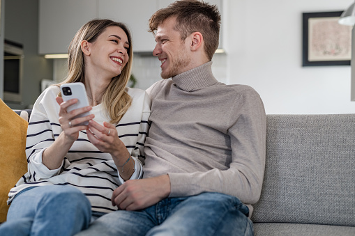 Young couple relaxing on the couch at home and using smart phone. Lifestyle and technology.